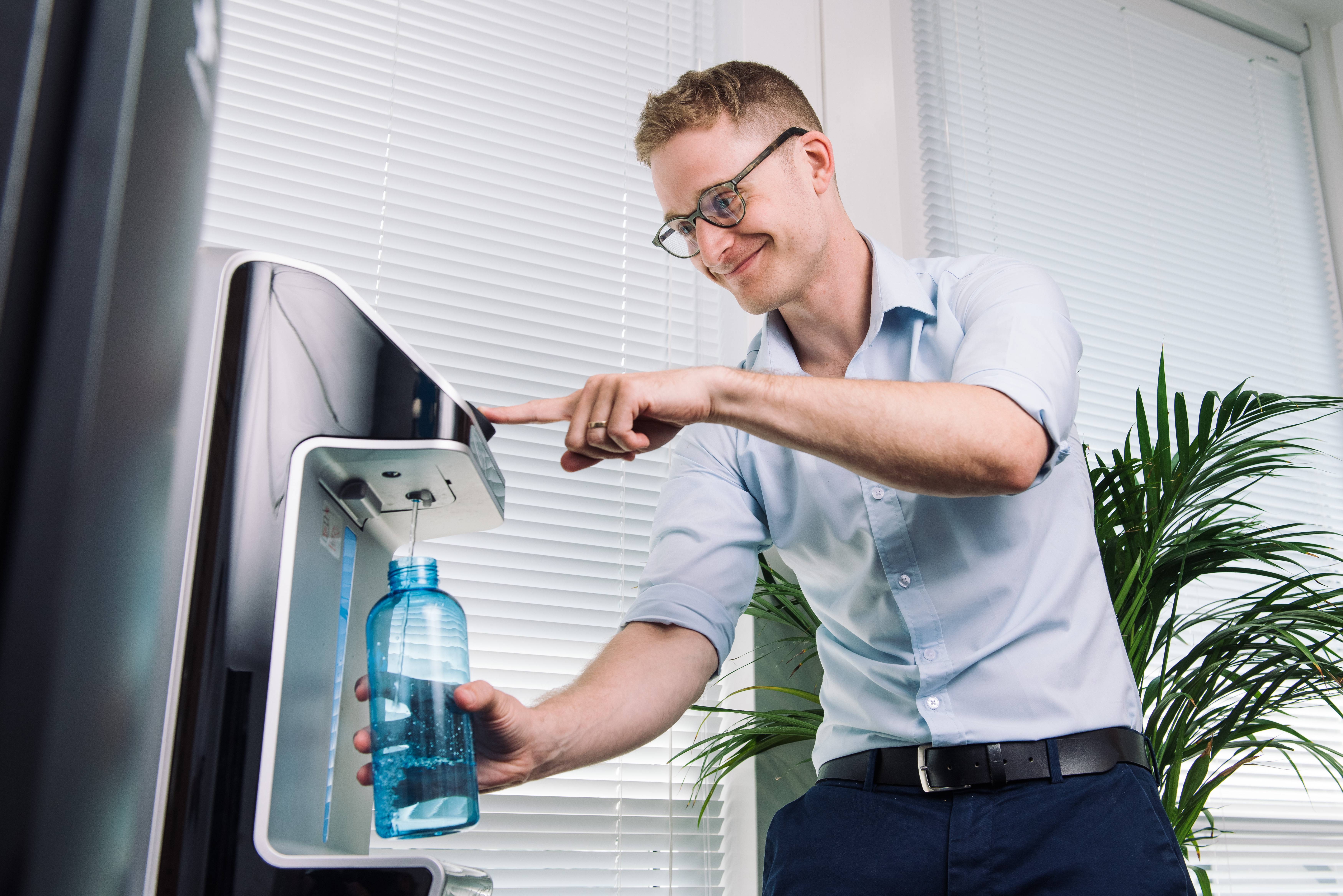Werknemer vult een waterfles bij een waterdispenser om gehydrateerd op het werk te blijven.